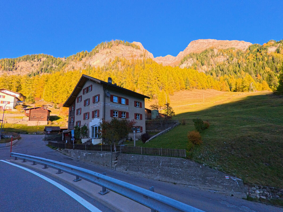 Eine ausgepraegte Strassenkurve verlaeuft vor einem Wohnhaus am Hang von Ferrera (7444, Kanton Graubünden).