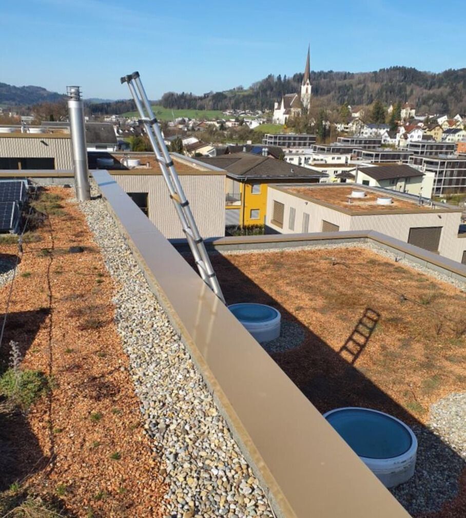 In Feuerthalen (8245, Kanton Zürich) zeigt das Bild einen Blick von einem Dach, auf dem eine Leiter, ein Kamin und zwei runde Behälter zu sehen sind, mit einem schönen Blick auf die Stadt und die Kirche im Hintergrund.