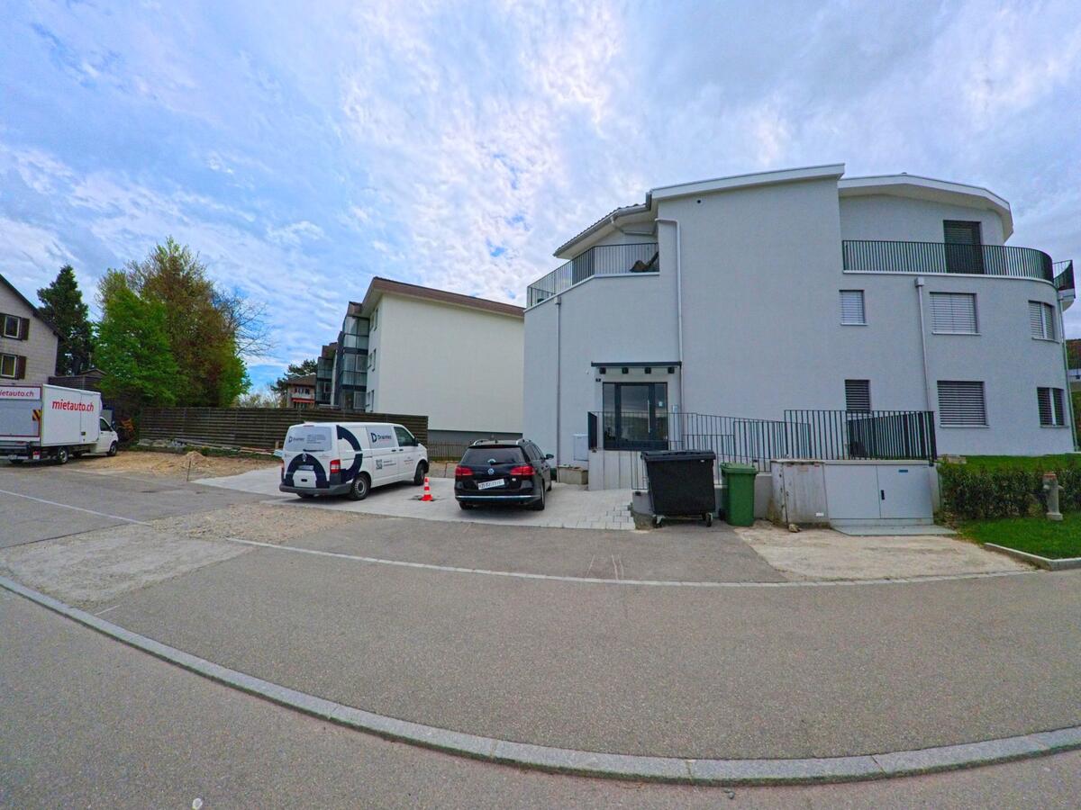 In Feuerthalen im PLZ-Bereich 8245 im Kanton Zürich steht ein modernes Mehrfamilienhaus mit abgerundeten Balkonen und angrenzendem Parkplatz an einer ruhigen Seitenstrasse.