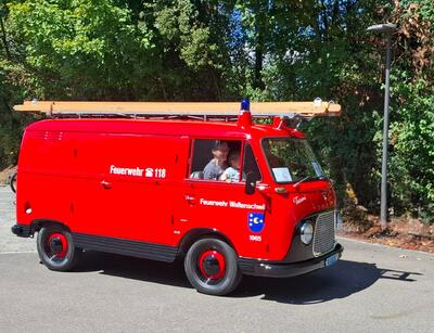 Ein rotes Feuerwehrfahrzeug des Feuerwehrvereins Waltenschwil mit aufgesetzter Leiter steht in Waltenschwil (5622, Kanton Aargau) vor dichtem Grün im Sonnenlicht.