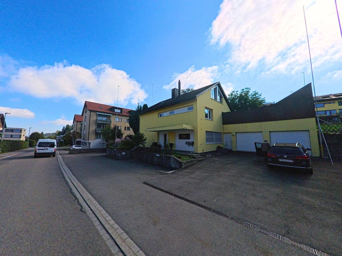 Vor einem gelb gestrichenen Einfamilienhaus öffnet sich eine kleine Zufahrt in Feusisberg (8835, Kanton Schwyz).