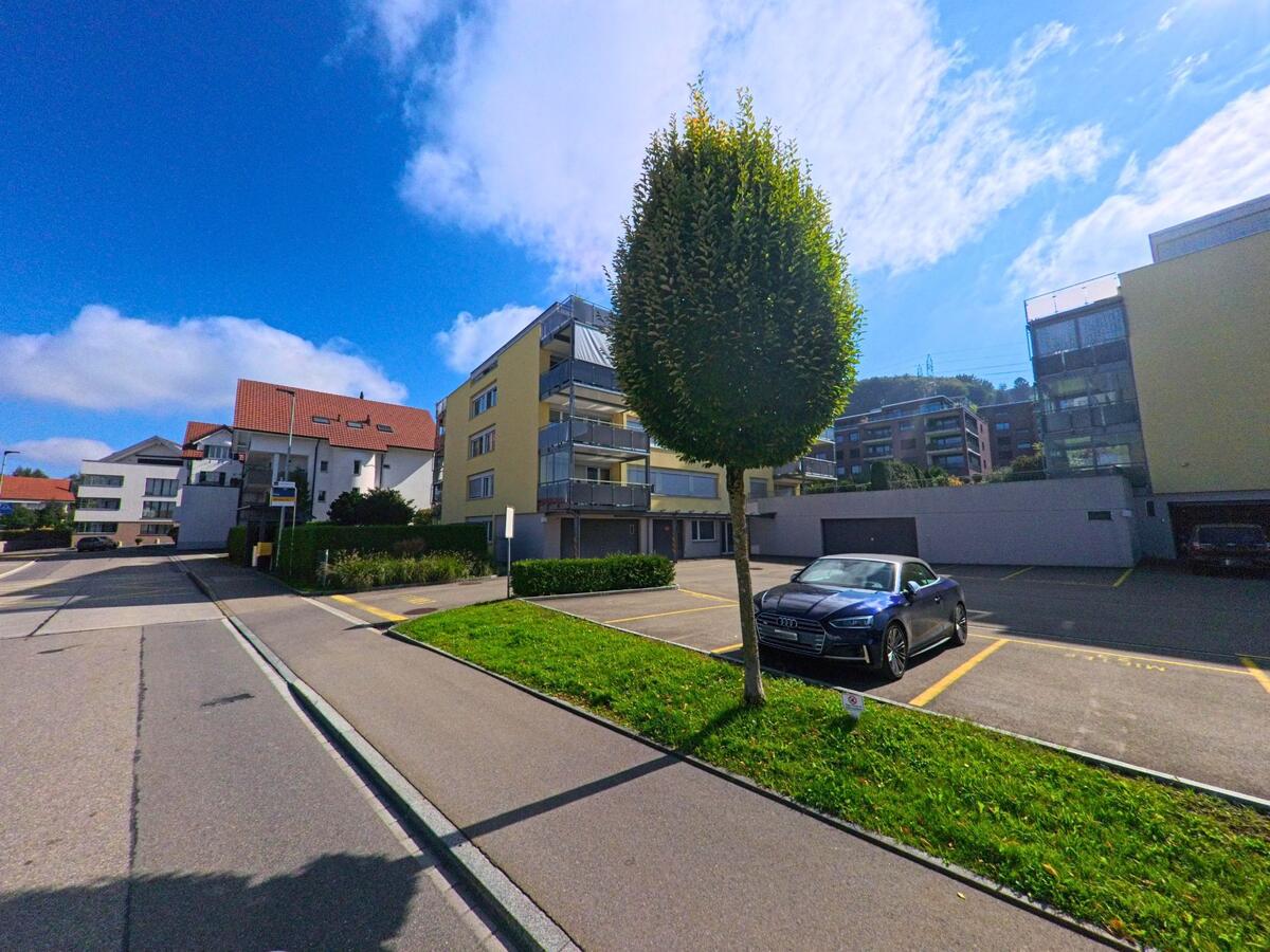 Zwischen Bäumen und Mehrfamilienhäusern verläuft eine ruhige Wohnstrasse in Feusisberg (8835, Kanton Schwyz).