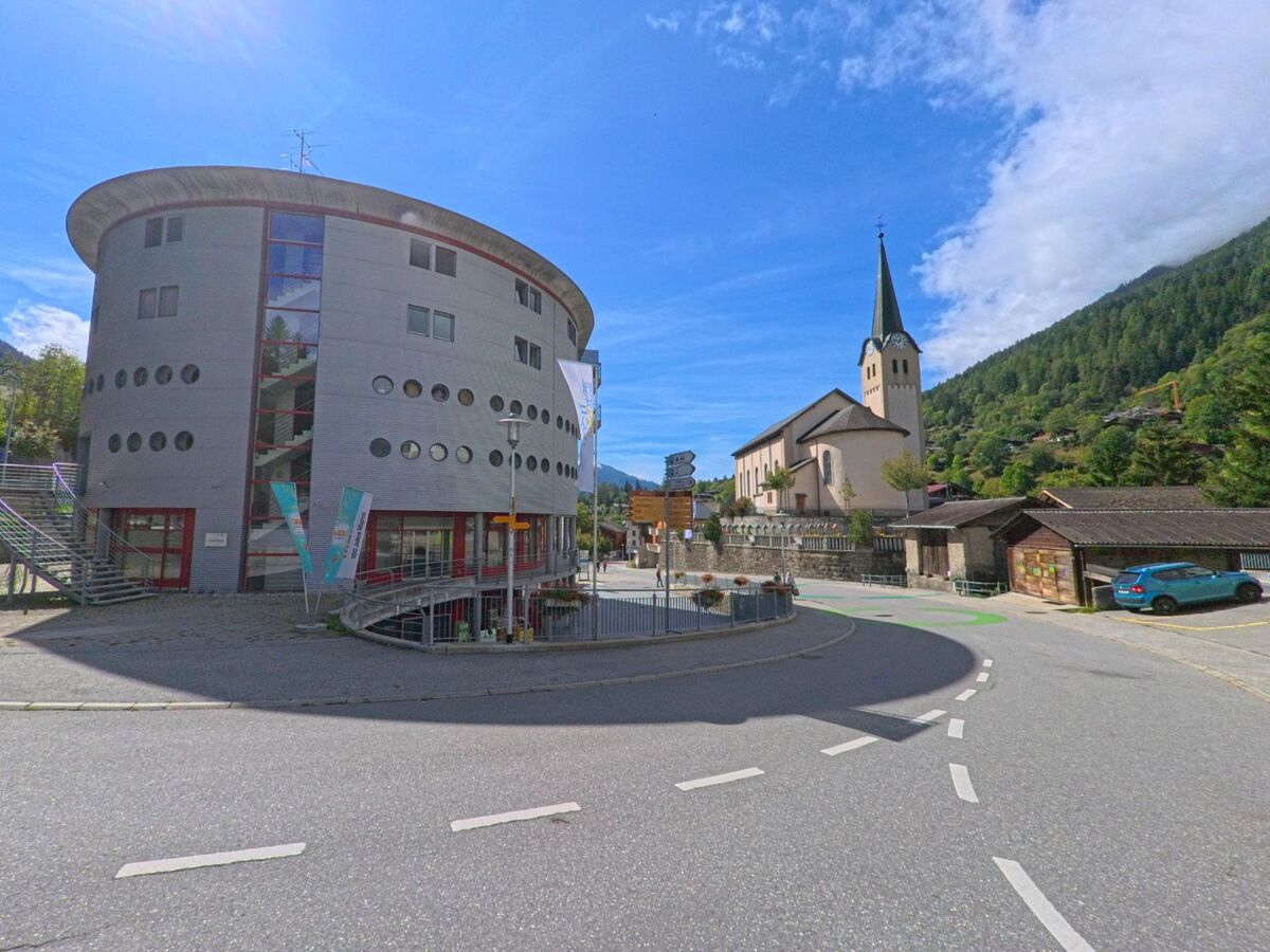 Im Zentrum von Fiesch (3984, Kanton Wallis) steht ein rundes modernes Gebaeude neben der Kirche mit markantem Glockenturm.