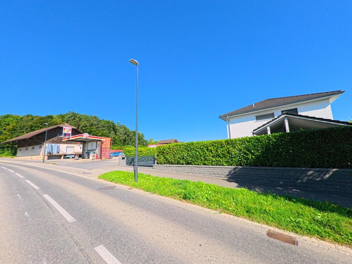 Am Ortsrand von Finsterhennen (2577, Kanton Bern) stehen ein modernes Wohnhaus hinter einer Hecke und eine Lagerhalle mit Firmenlogo an der Strasse.