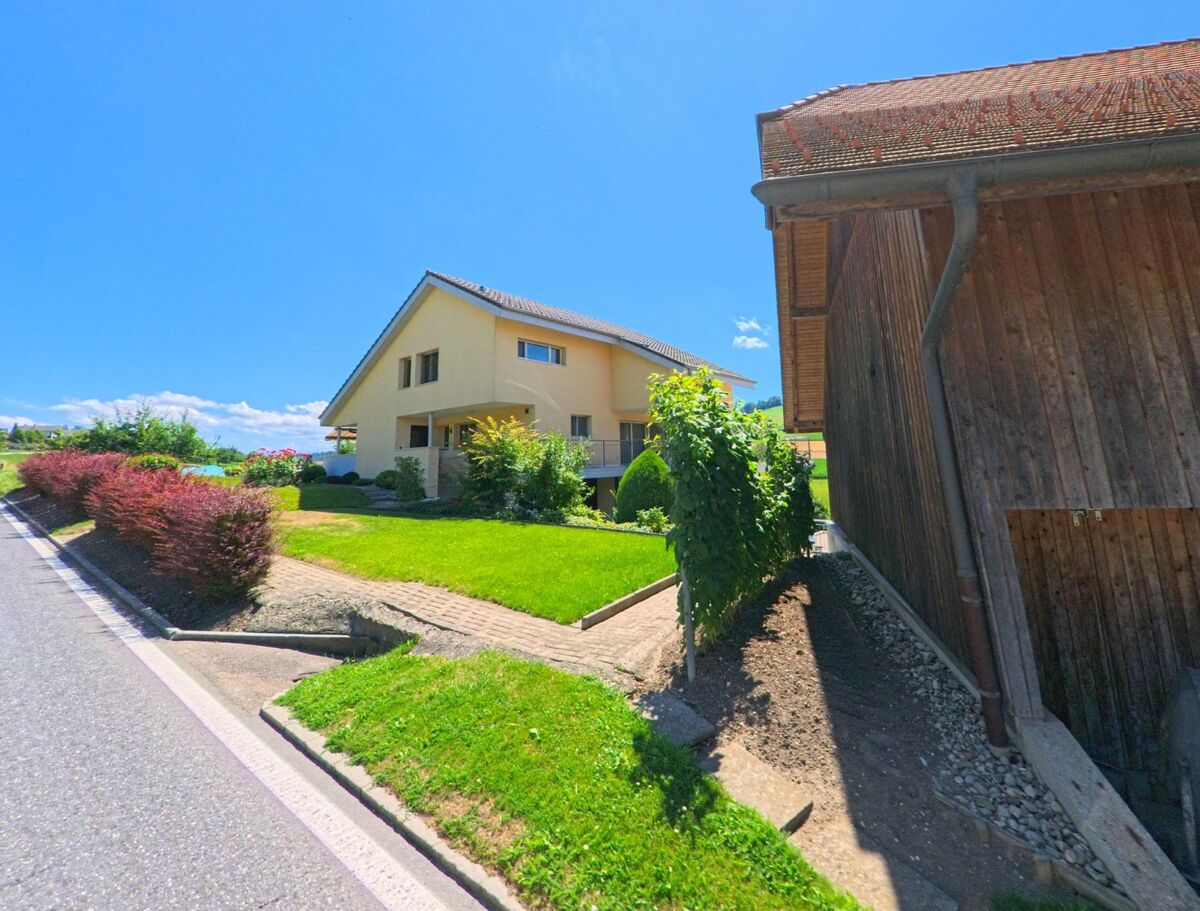 In einem ruhigen Wohngebiet von Fischbach (6145, Kanton Luzern) steht ein modernes Einfamilienhaus mit gepflegtem Garten neben einer traditionellen Holzscheune.
