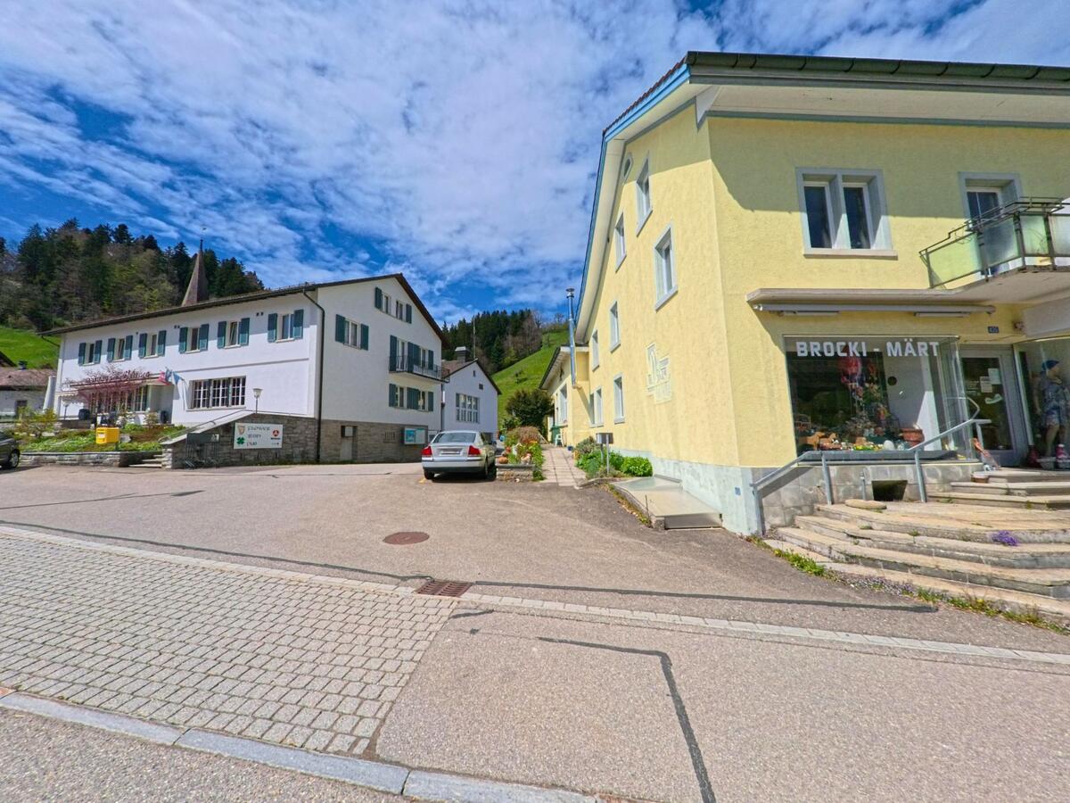 In Fischenthal im PLZ-Gebiet 8497 im Kanton Zürich befinden sich ein gelbes Geschäftshaus mit dem Brocki-Märt und ein Verwaltungsgebäude mit Fahnen an einem kleinen Platz.