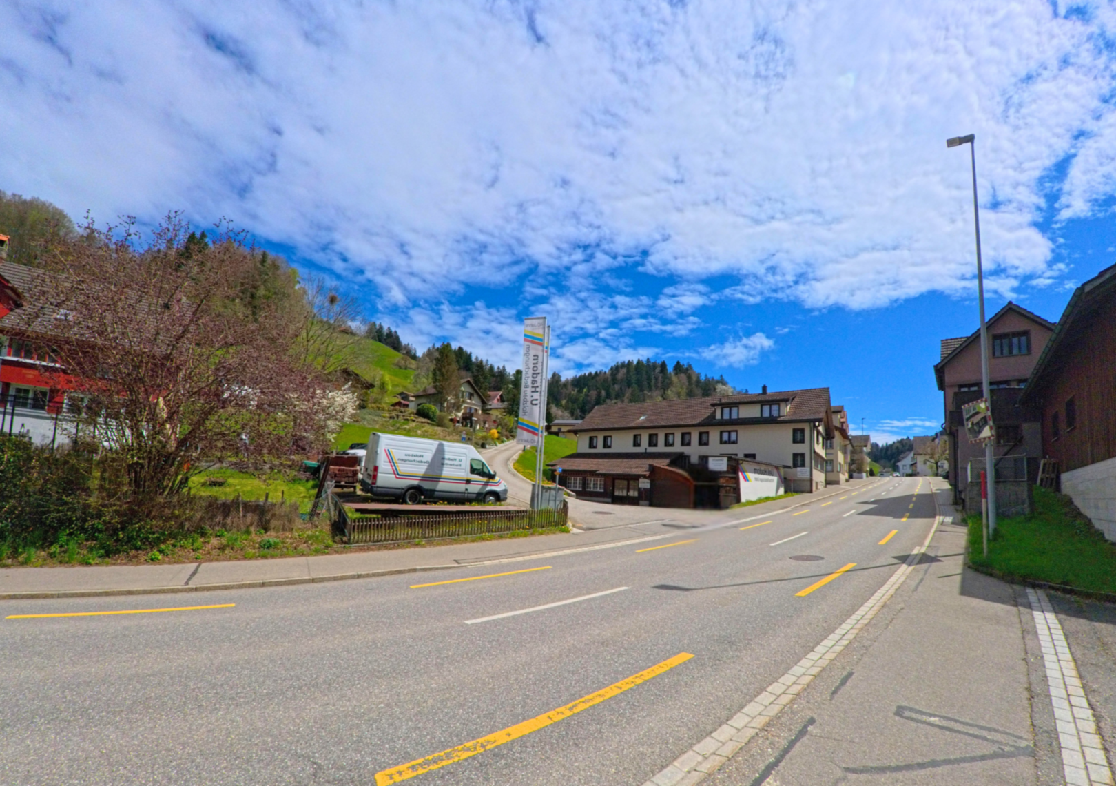 In Fischenthal im PLZ-Gebiet 8497 im Kanton Zürich verläuft eine Hauptstrasse durch den Ortskern, flankiert von Gewerbebauten und Wohnhäusern am Hang.