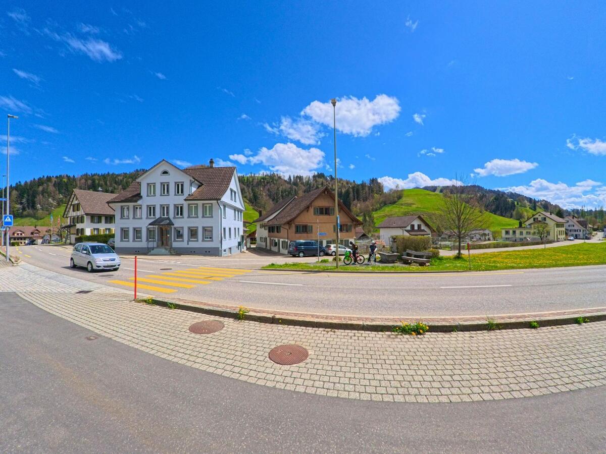 In Fischenthal im PLZ-Gebiet 8497 im Kanton Zürich kreuzen sich zwei Strassen vor einem weissen Wohnhaus mit Zebrastreifen, umgeben von ländlicher Hügellandschaft.