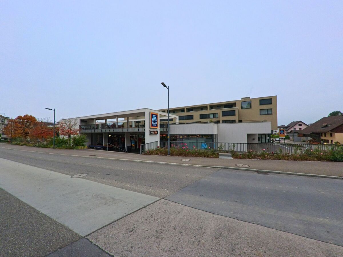 Das moderne Gebäude eines Supermarkts in Fislisbach (5442, Kanton Aargau) liegt an einer Hauptstrasse und ist von herbstlich gefärbten Bäumen umgeben.