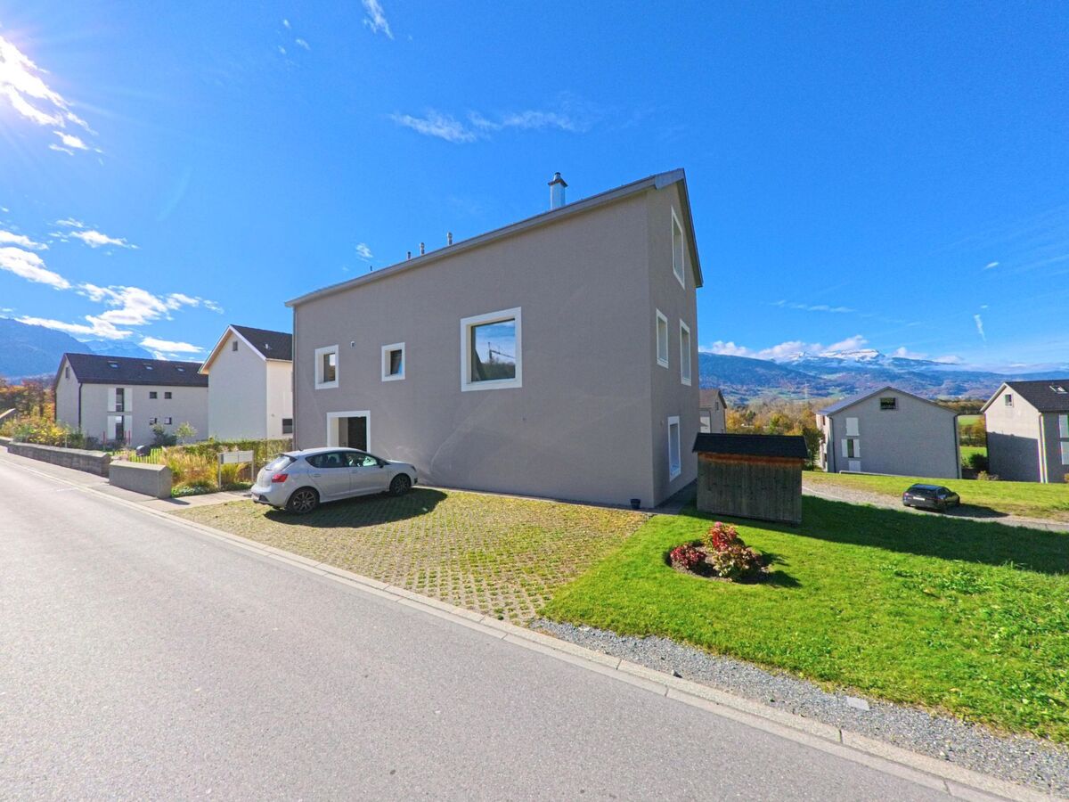 Vor modernen Wohnhäusern mit gepflegten Grünflächen zeigt sich ein ruhiges Quartier von Fläsch (7306, Kanton Graubünden) mit weiter Sicht auf die umliegende Landschaft.