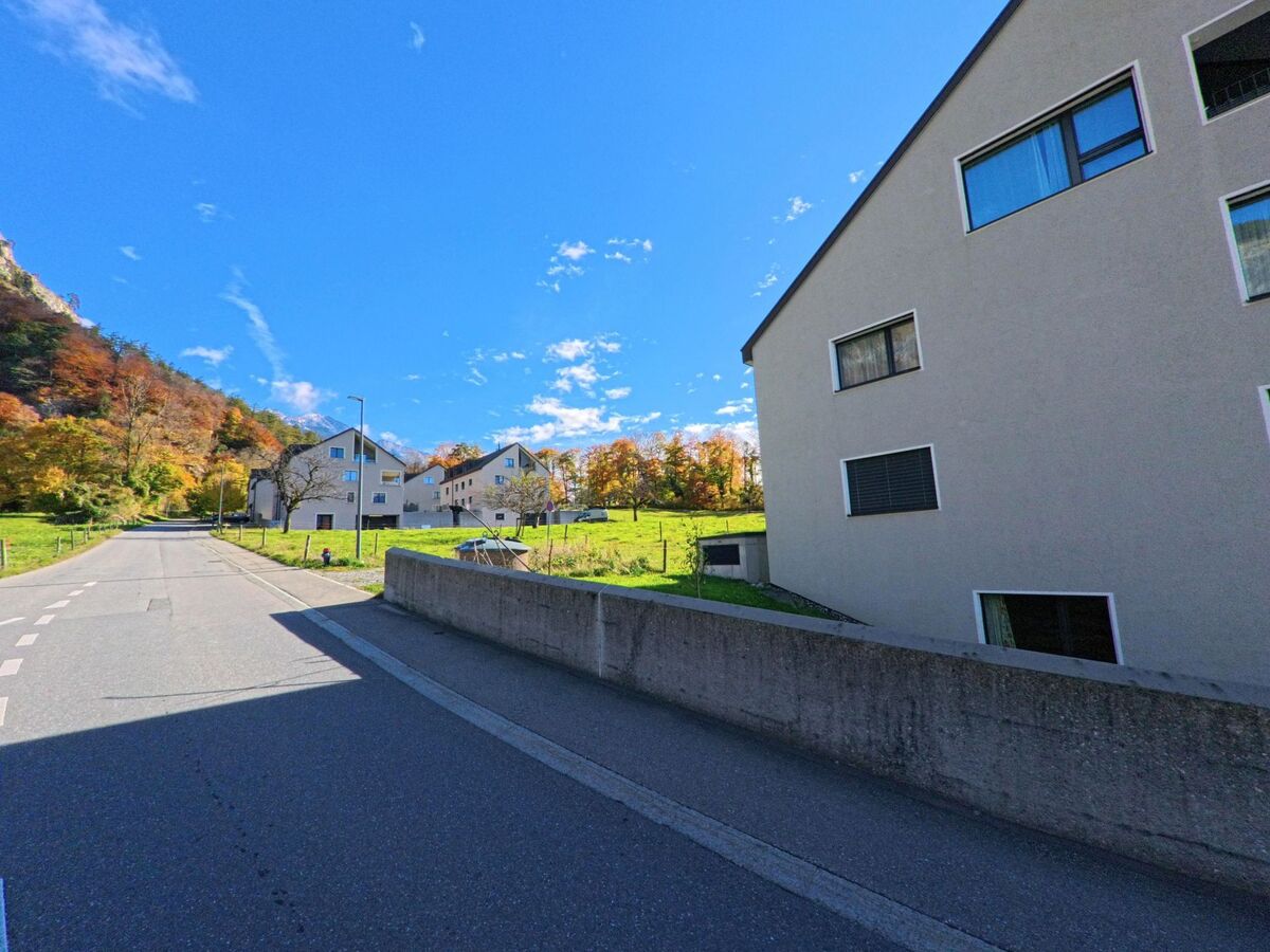 Entlang einer ruhigen Wohnstrasse mit modernen Mehrfamilienhäusern und angrenzenden Grünflächen zeigt sich ein Quartier von Fläsch (7306, Kanton Graubünden) im herbstlichen Licht.