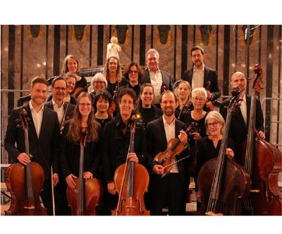 Das Flawiler Kammerorchester aus Flawil (9230, Kanton St. Gallen) posiert nach einem Konzert in eleganter Abendkleidung, umgeben von klassischen Instrumenten.