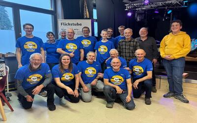 Das Team der Flickstuba Widnau posiert in Widnau (9443, Kanton St. Gallen) gemeinsam in blauen Vereinsshirts vor einer Bühne.