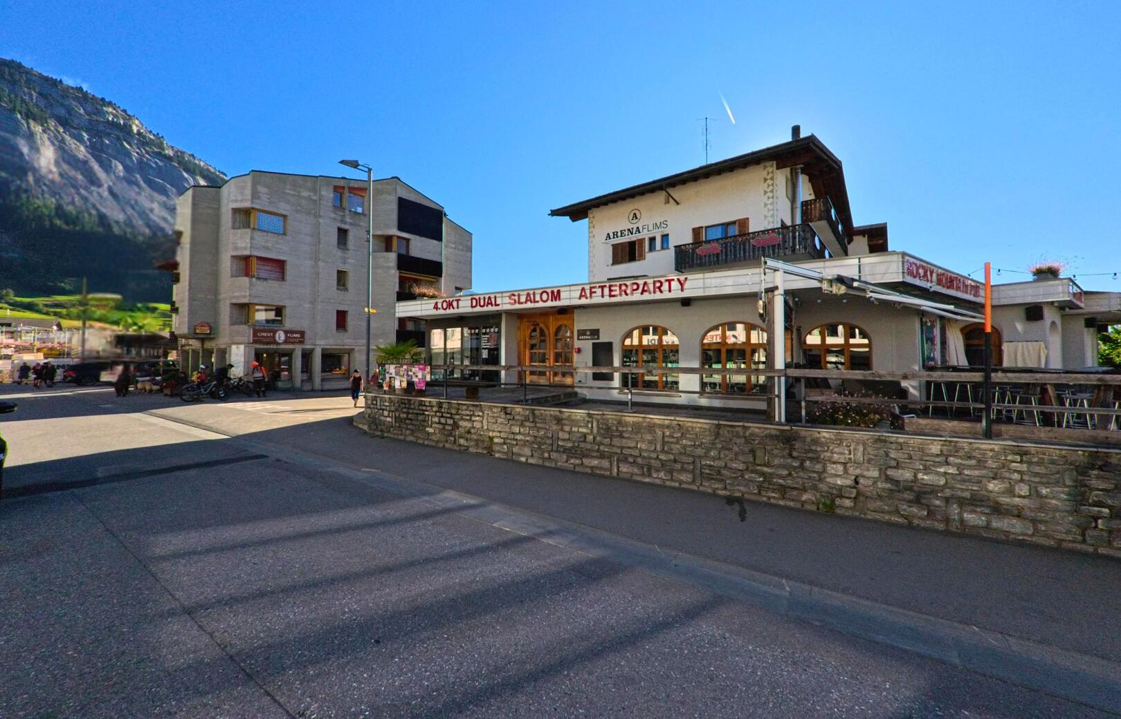 Im Zentrum von Flims (7017, Kanton Graubuenden) steht das Gebaeude der Arena Flims neben modernen Wohnhaeusern vor der steilen Bergwand.