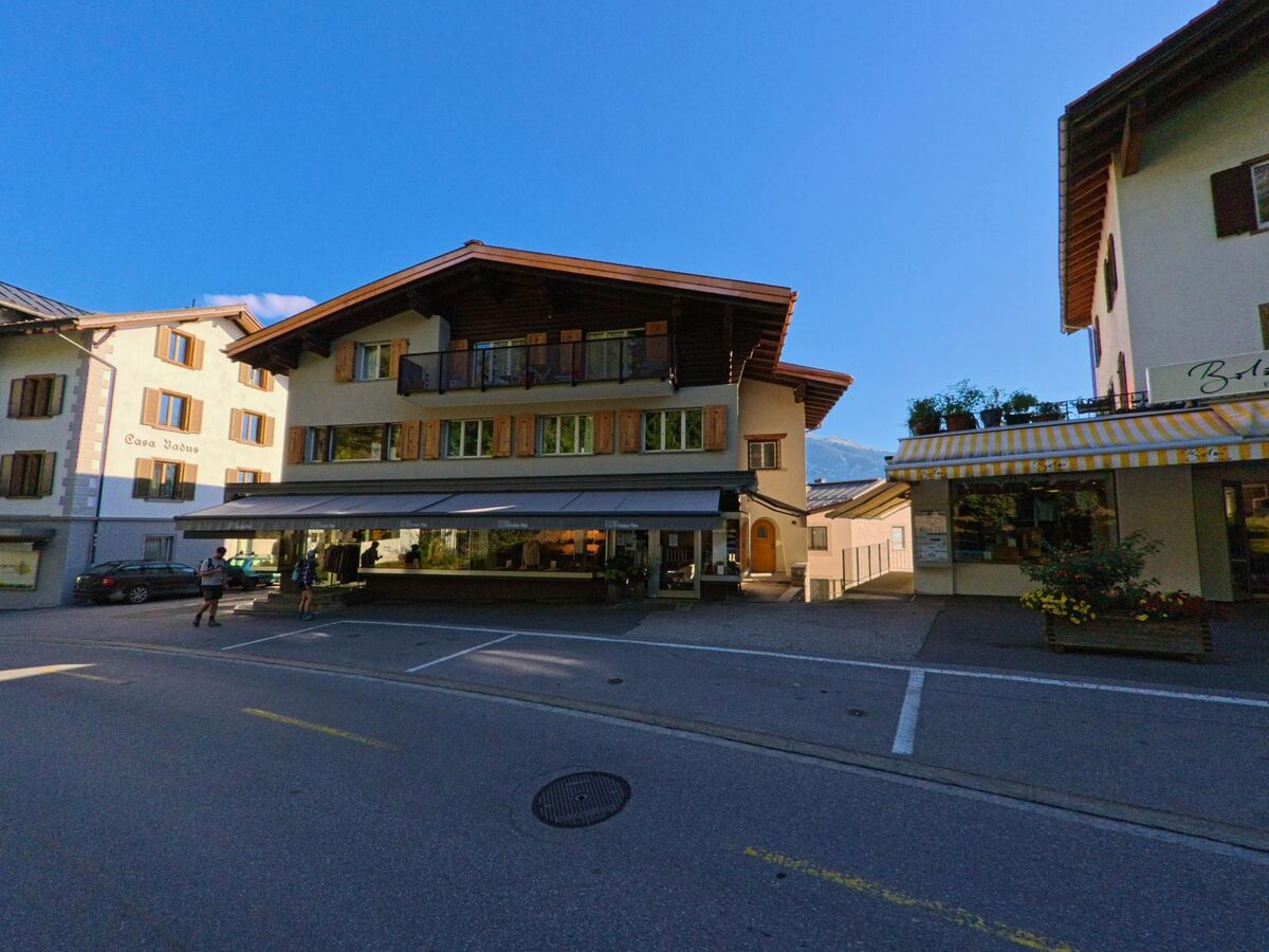 Zwischen traditionellen Gebaeuden in Flims (7018, Kanton Graubuenden) befindet sich ein Haus mit Holzbalkonen und Ladenfront unter einer grossen Markise.
