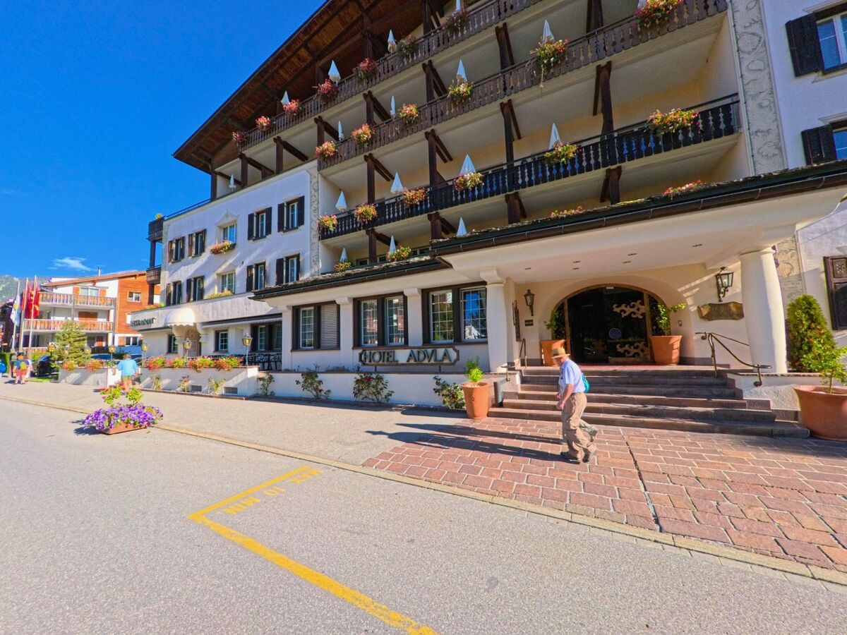 Das Hotel Adula in Flims (7018, Kanton Graubuenden) zeigt eine traditionelle Fassade mit Balkonen und Blumenschmuck an einer sonnigen Strasse.