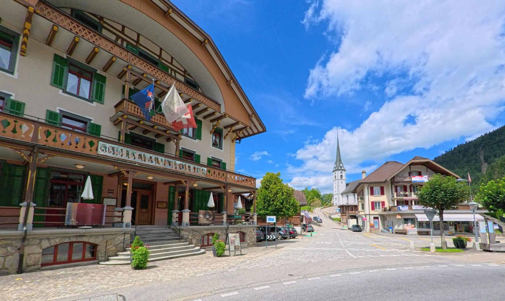 Im Zentrum von Flühli (6173, Kanton Luzern) dominiert das historische Hotel Kurhaus mit Veranda die gepflasterte Platzsituation vor der Kirche und angrenzenden Wohnhäusern.