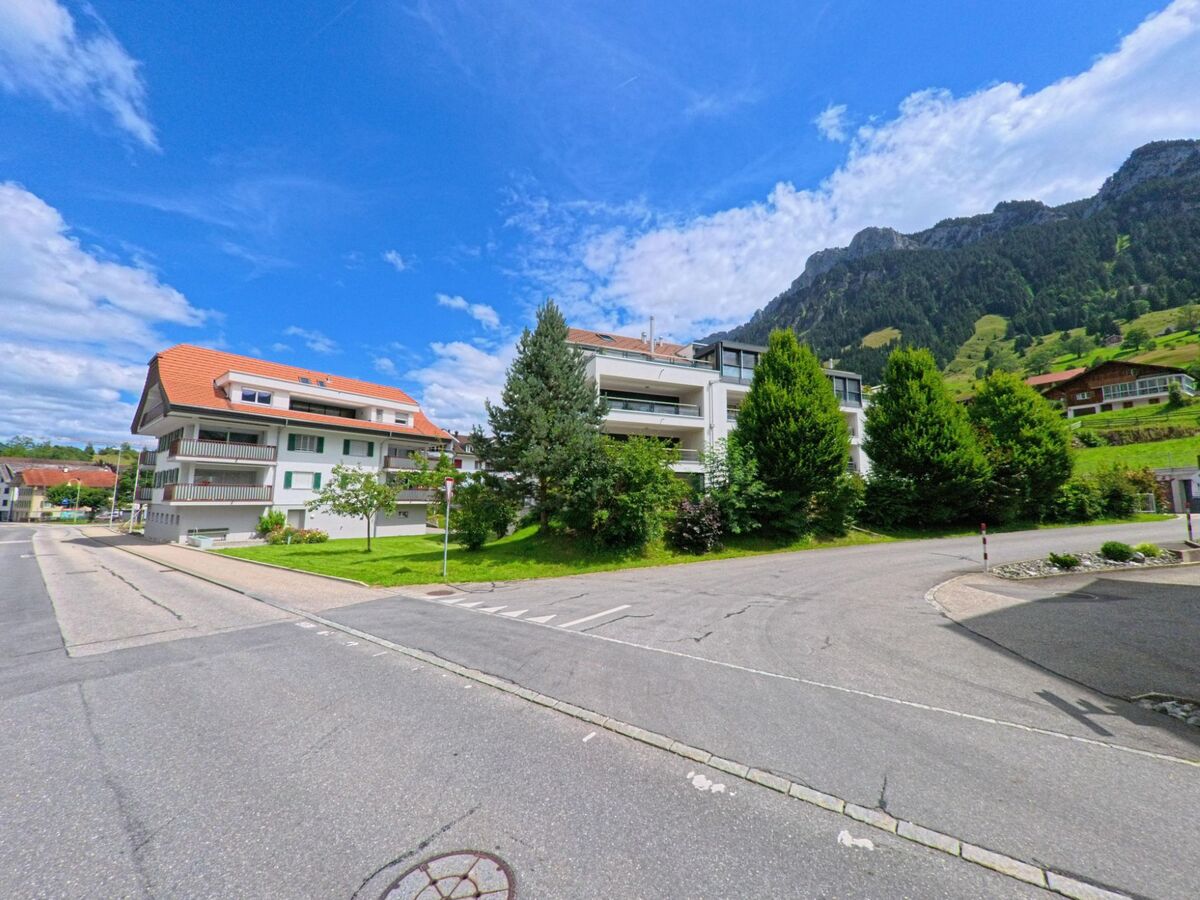 In Flühli (6173, Kanton Luzern) stehen moderne Wohnhäuser mit Gartenanlagen vor bewaldeten Berghängen am ruhigen Dorfrand.