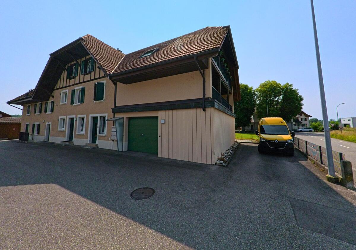 In Flumenthal (4534, Kanton Solothurn) steht ein traditionelles Wohnhaus mit gruenen Fensterlaeden und integriertem Garagenbereich nahe einer Durchgangsstrasse.