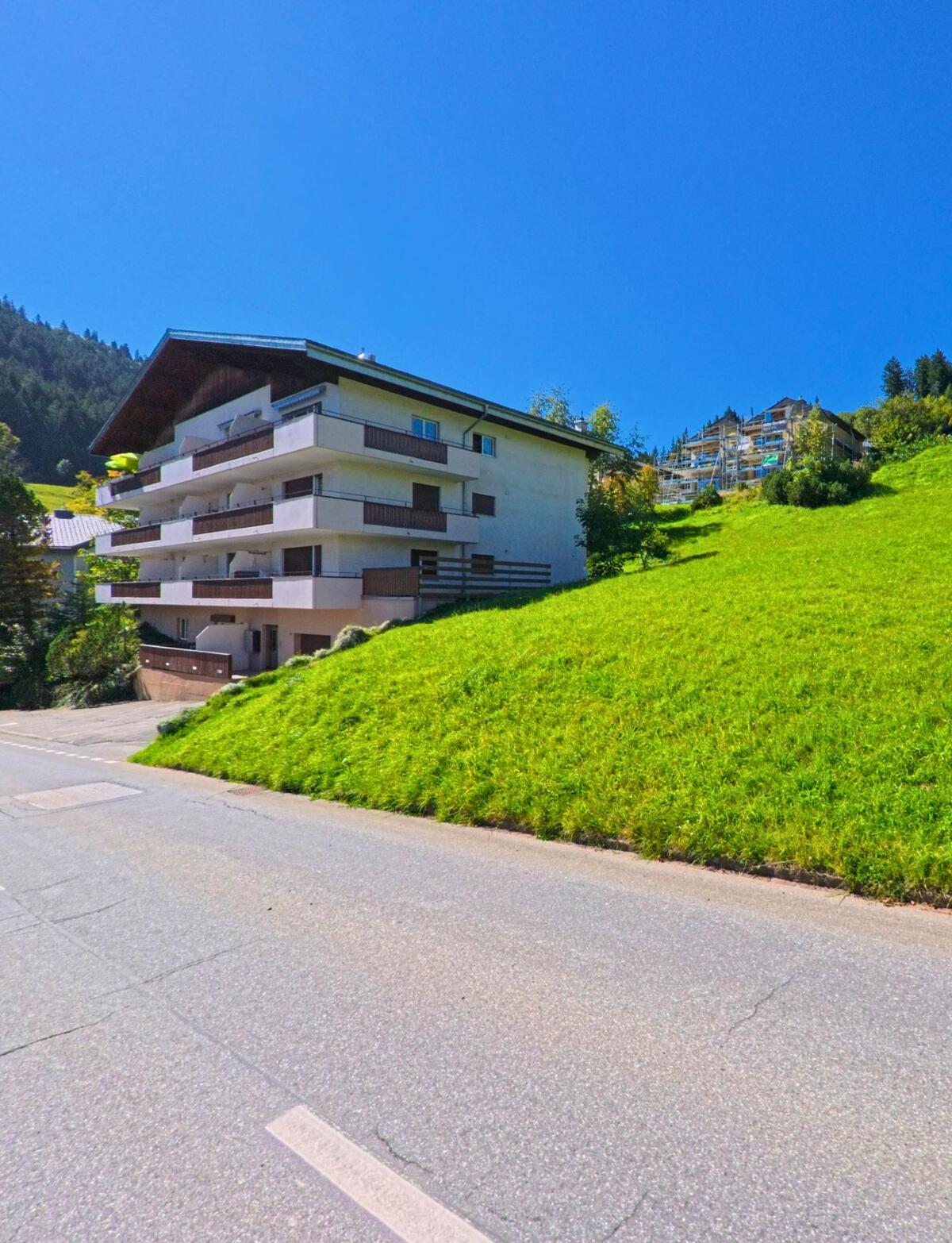 Ein Mehrfamilienhaus mit grossen Balkonen steht in Flums (8897, Kanton St. Gallen) an einem sonnigen Hang mit Blick auf die bewaldeten Berghaenge.