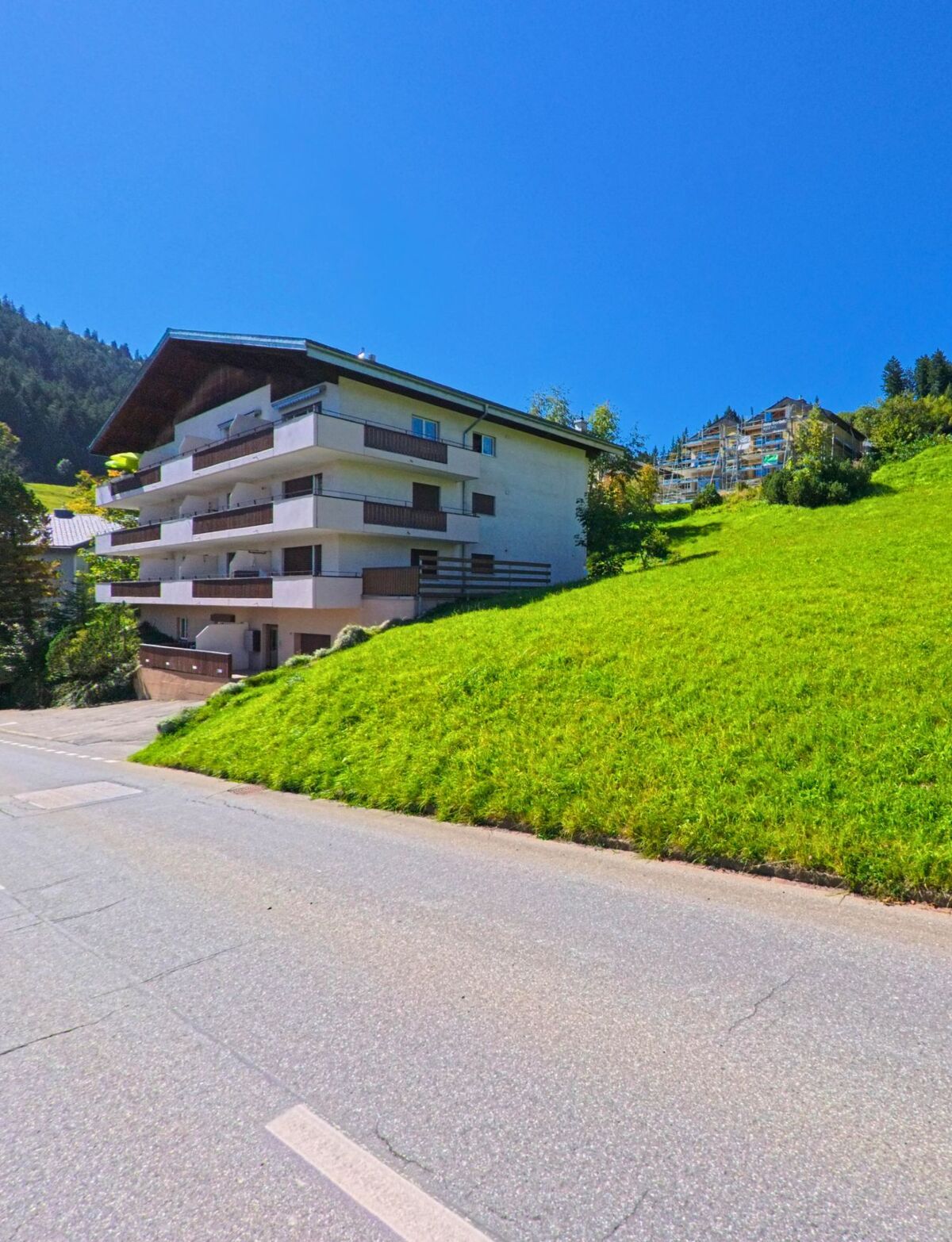 Ein Mehrfamilienhaus mit grossen Balkonen steht in Flums (8897, Kanton St. Gallen) an einem sonnigen Hang mit Blick auf die bewaldeten Berghaenge.
