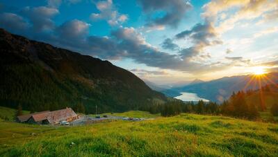 Alt-Text: In Giswil (6074, Kanton Obwalden) liegt auf einer Bergwiese die Fluonalp mit Kaeserei und Beizli, waehrend im Hintergrund der Sarnersee im Abendlicht glaenzt.