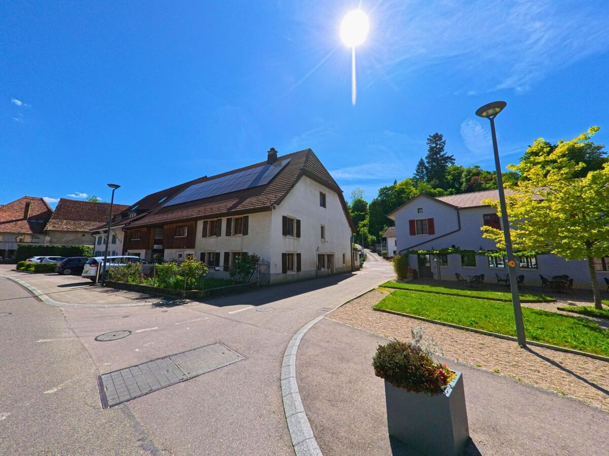 In einem sonnigen Wohnviertel von Fontenais (2902 im Kanton Jura) grenzen modernisierte Häuser mit Solarpanels an eine kleine Platzanlage mit Sitzgelegenheiten.