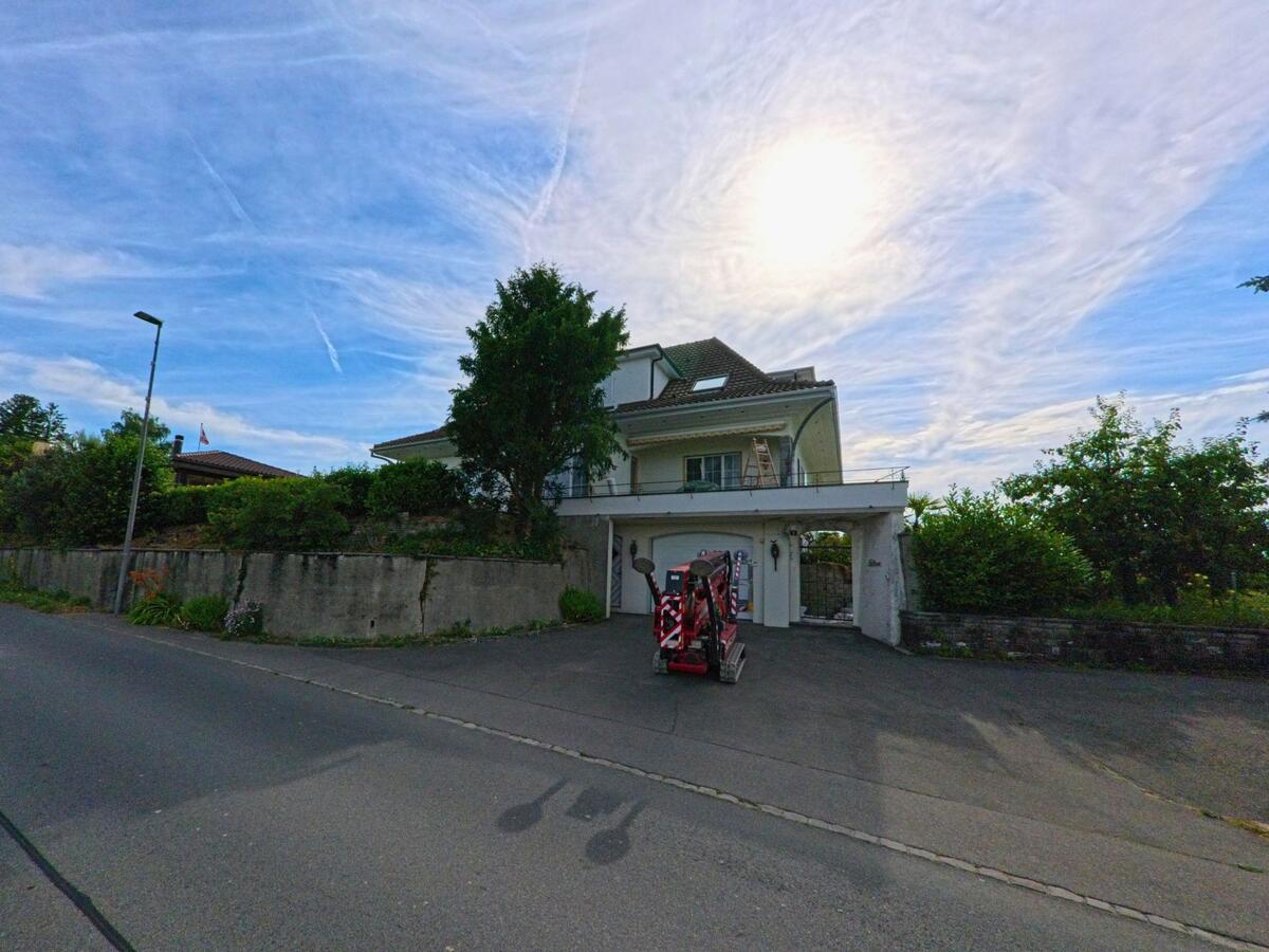 In Fräschels (3284, Kanton Freiburg) steht ein modernes Wohnhaus mit Garage und Balkon oberhalb einer kleinen Baustellenzufahrt an einer ruhigen Quartierstrasse.