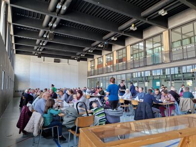 In Summaprada 7421 im Kanton Graubünden sitzen zahlreiche Menschen in einer grossen Halle an langen Tischen bei einem gemeinsamen Anlass.