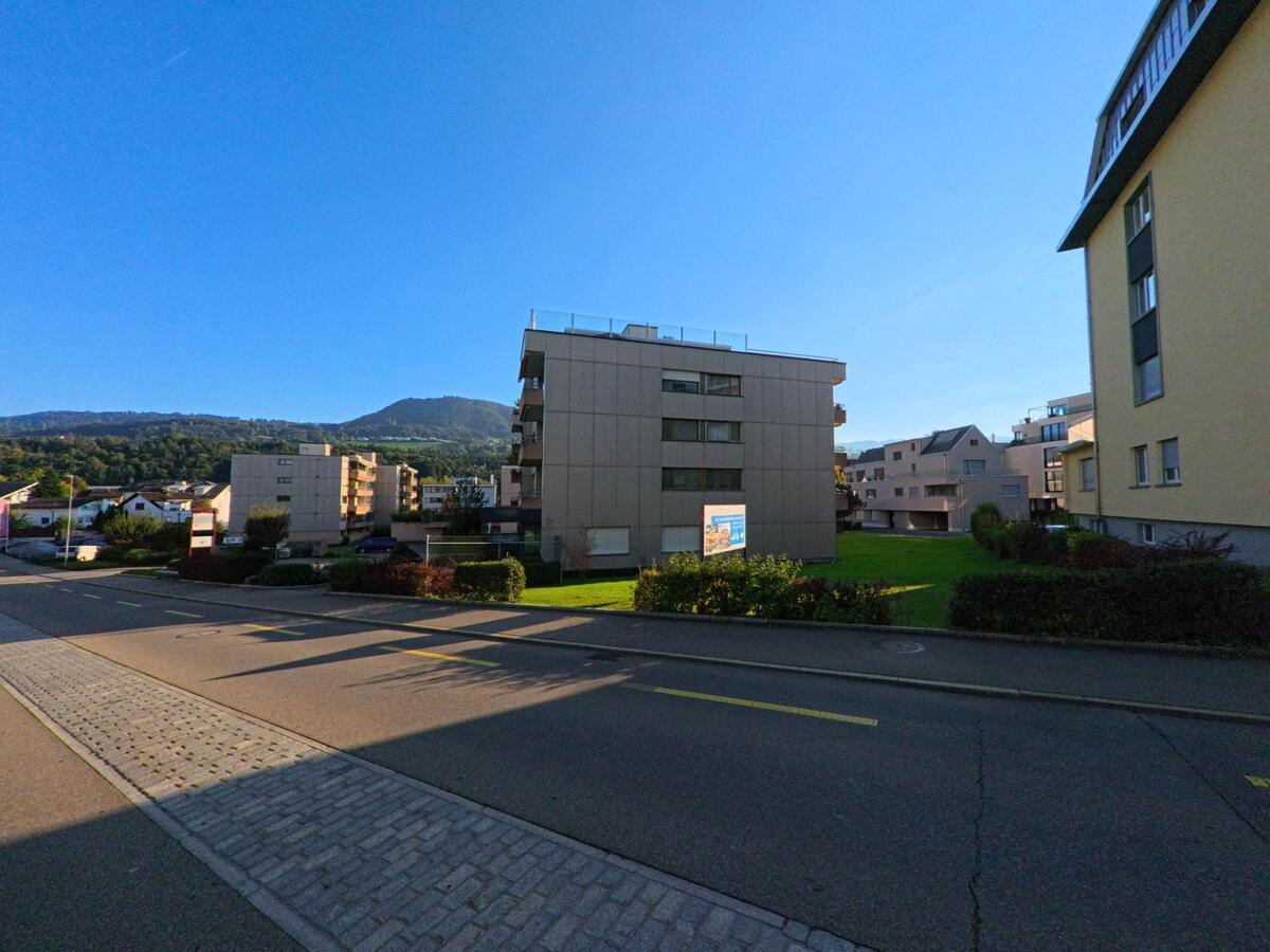 Hinter den Wohnbauten in Freienbach (8808, Kanton Schwyz) oeffnet sich ein begruenter Innenbereich, waehrend im Hintergrund bewaldete Huegel die Szenerie praegen.
