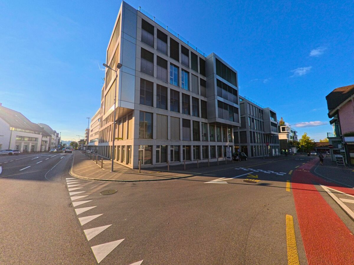 Ein modernes Eckgebaeude in Freienbach (8808, Kanton Schwyz) wirft lange Schatten auf die Strassenkreuzung, an der ein roter Veloweg vorbeifuehrt.