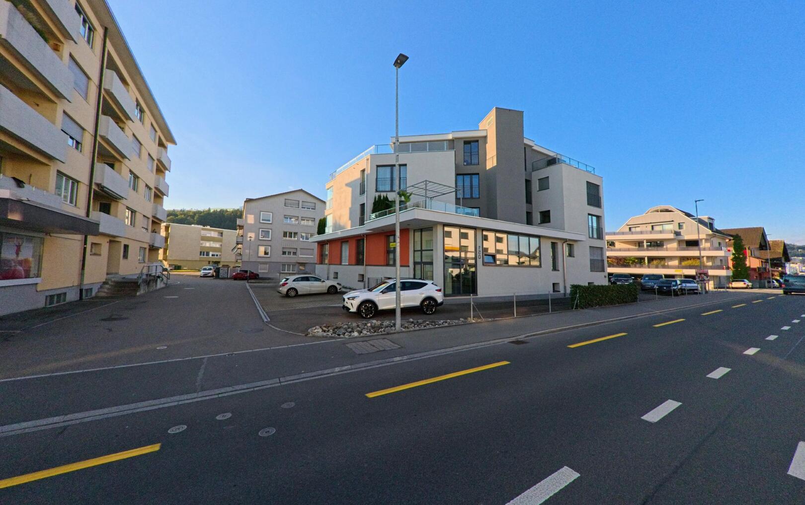 In Freienbach (8808, Kanton Schwyz) saeumen moderne Wohnhaeuser eine breite Strasse, deren klare Linien im Abendlicht deutliche Schatten auf den Asphalt werfen.