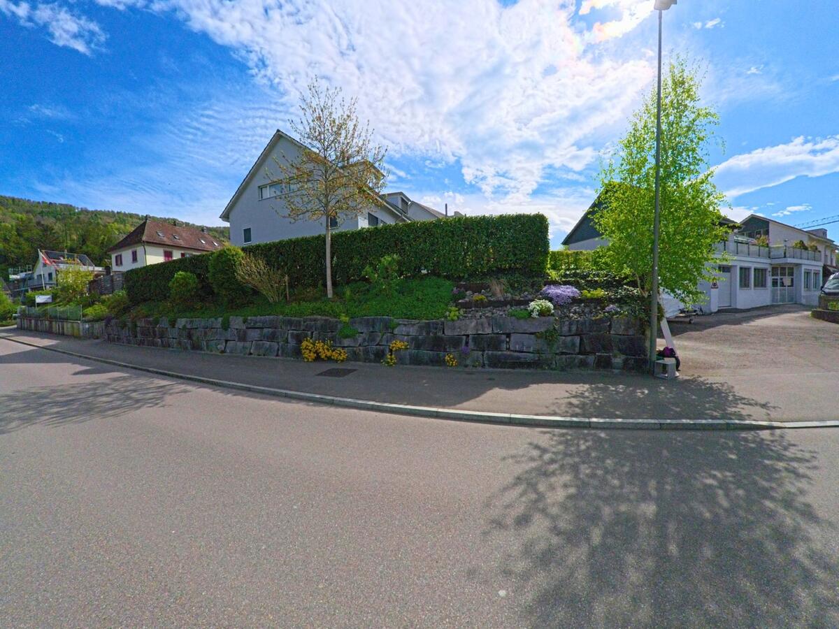 In Freienstein-Teufen (PLZ 8427, Kanton Zürich) stehen moderne Wohnhäuser auf einem leicht erhöhten Gelände, eingefasst von Natursteinmauern und gepflegter Bepflanzung.