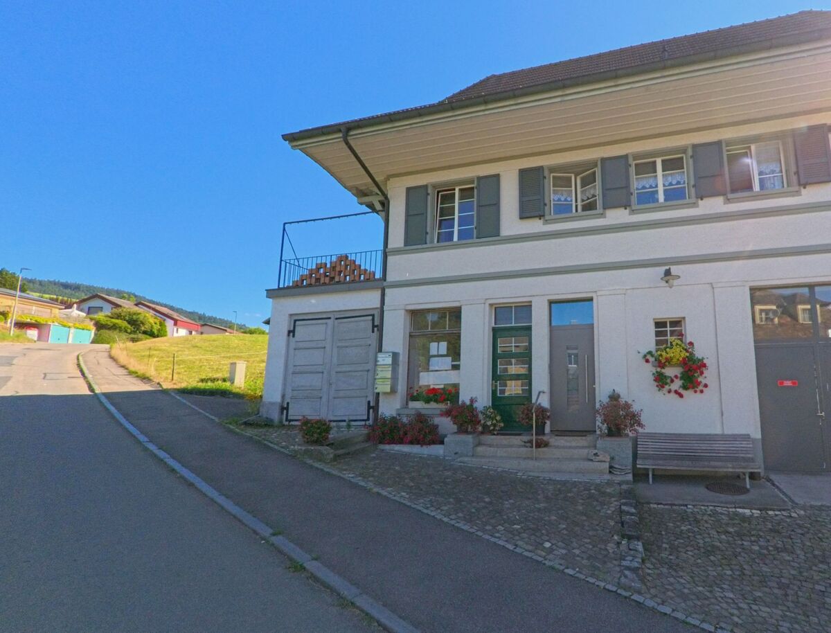 In Freimettigen (3510, Kanton Bern) steht ein schlichtes zweistoeckiges Gebaeude mit gruenen Fensterlaeden, Blumenkaesten und Holzstapel an einer ansteigenden Quartierstrasse.