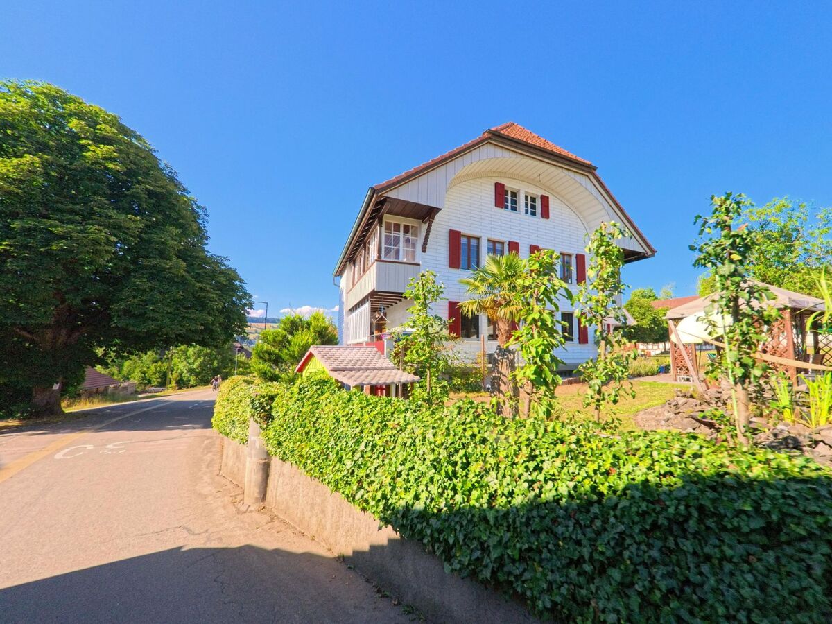 In Freimettigen (3510, Kanton Bern) steht ein gepflegtes Wohnhaus mit roten Fensterlaeden an einer Kurve, umgeben von einem Garten mit Pavillon und dichter Bepflanzung.