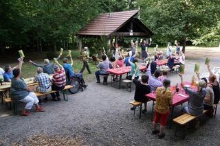 In Burgdorf (3401, Kanton Bern) sitzen zahlreiche Personen an Tischen im Freien und nehmen gemeinsam an einem geselligen Anlass im Wald teil.