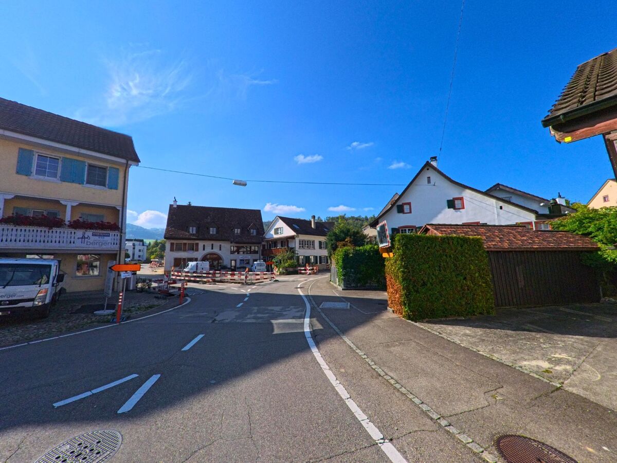 In Frenkendorf (4402, Kanton Basel-Landschaft) fuehrt eine kurvige Strasse durch ein Quartier mit traditionellen Haeusern, waehrend im Zentrum Bauarbeiten sichtbar sind.