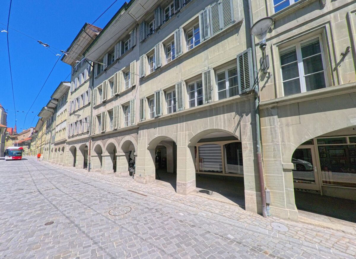 Eine gepflasterte Strasse in Fribourg (1700, Kanton Fribourg) wird von langen Arkadenhaeusern mit Fensterlaeden und Laubengaengen gesaeumt.