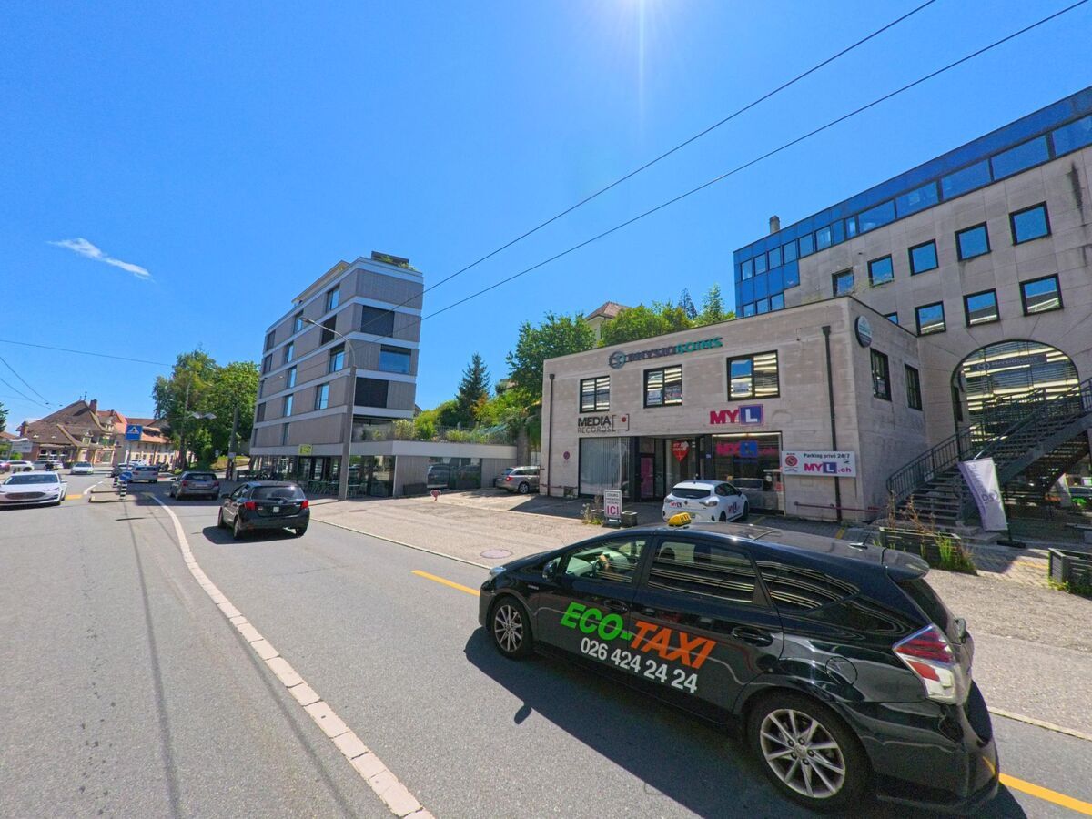 In Fribourg (1700, Kanton Fribourg) verläuft eine Strasse mit modernen Geschaeftsgebaeuden und einem Eco-Taxi im Vordergrund.