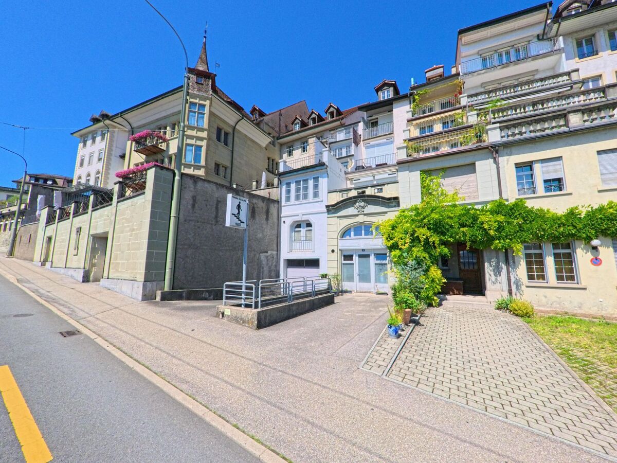 Mehrere Wohnhaeuser in Fribourg (1700, Kanton Fribourg) zeigen verzierte Fassaden, Balkone mit Blumen und begruente Eingangsbereiche an einer ansteigenden Strasse.