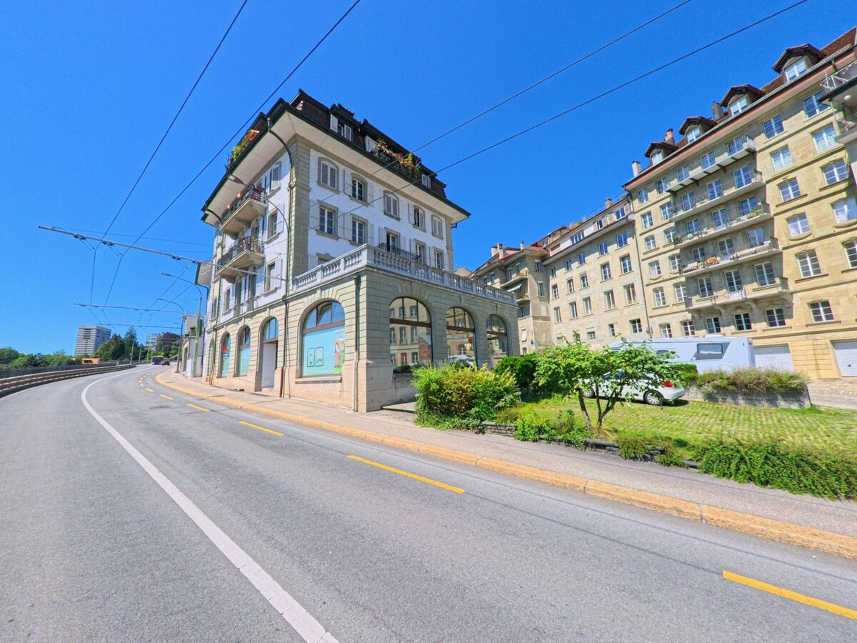 Eine ansteigende Strasse in Fribourg (1700, Kanton Fribourg) verläuft entlang mehrgeschossiger Wohnhaeuser mit Balkonen und Arkaden.