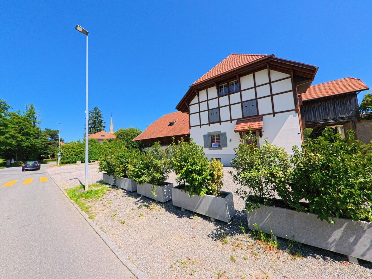 Ein traditionelles Fachwerkhaus mit roten Daechern steht in Fribourg (1722, Kanton Freiburg) an einer ruhigen Strasse mit Zebrastreifen.