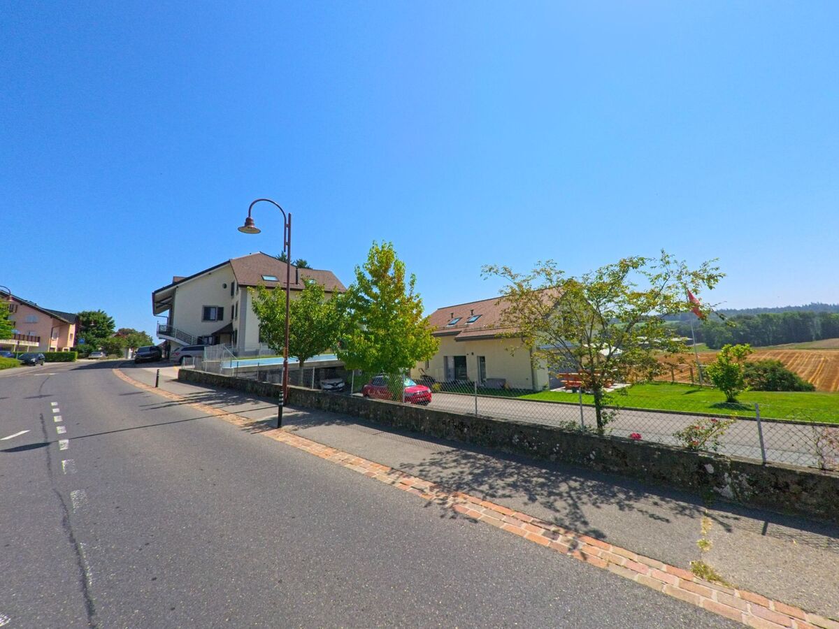 Am Rand von Froideville (1055, Kanton Waadt) stehen Wohnhaeuser neben einem Feld mit frisch gemähten Reihen.