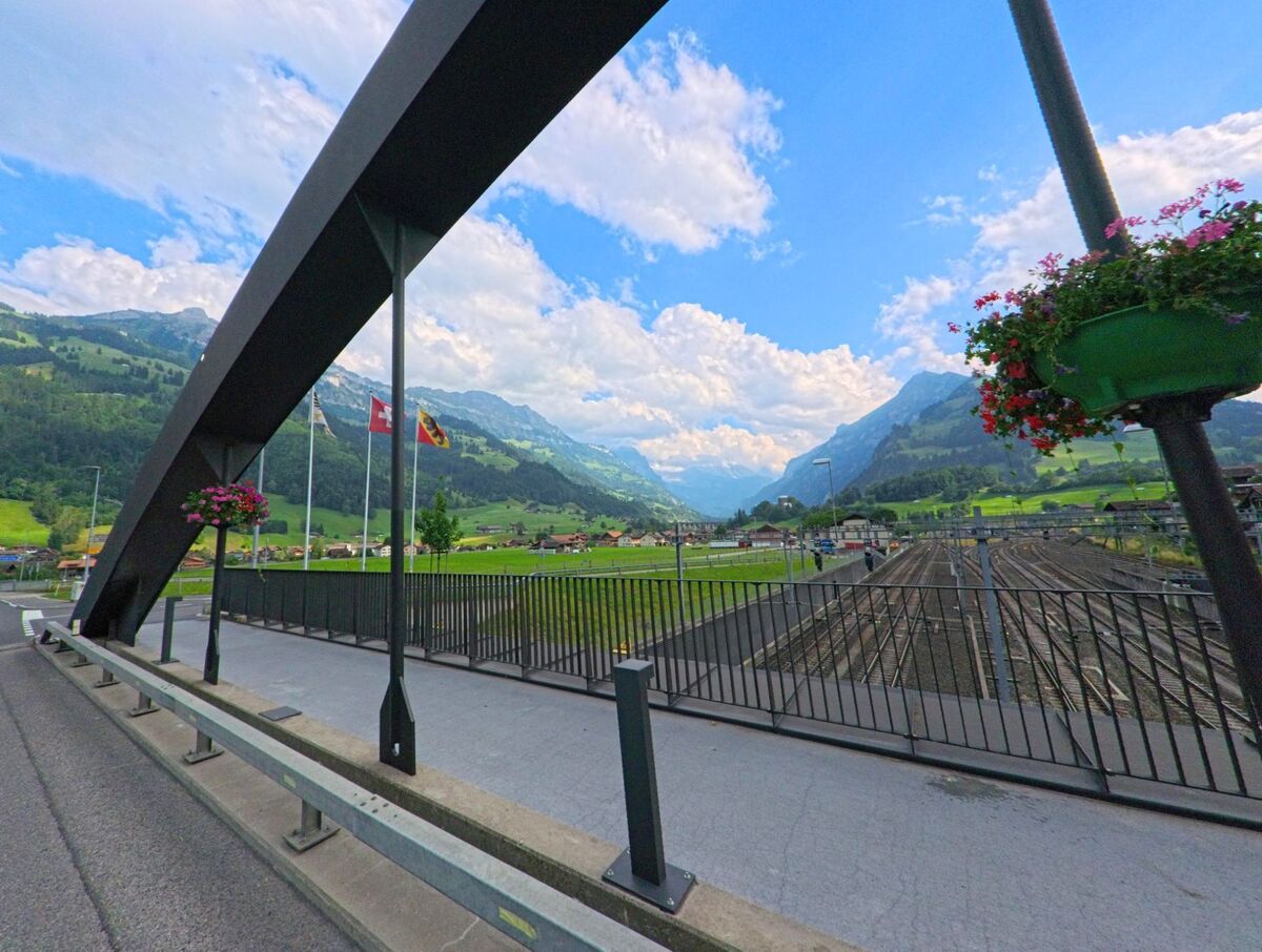 Von einer modernen Brücke in Frutigen (3714, Kanton Bern) aus eröffnet sich der Blick über das Gleisfeld des Bahnhofs, umrahmt von grünen Berghängen und einem weiten Tal.