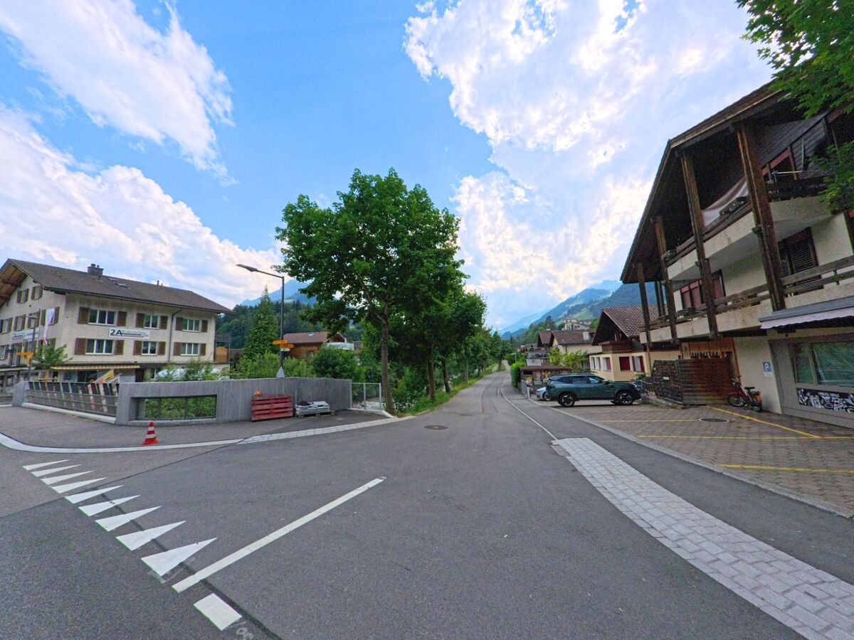 Eine ruhige Seitenstrasse in Frutigen (3714, Kanton Bern) verläuft zwischen Wohnhaeusern und Baeumen, eingerahmt von bewaldeten Haengen und einem weiten Blick ins Tal.