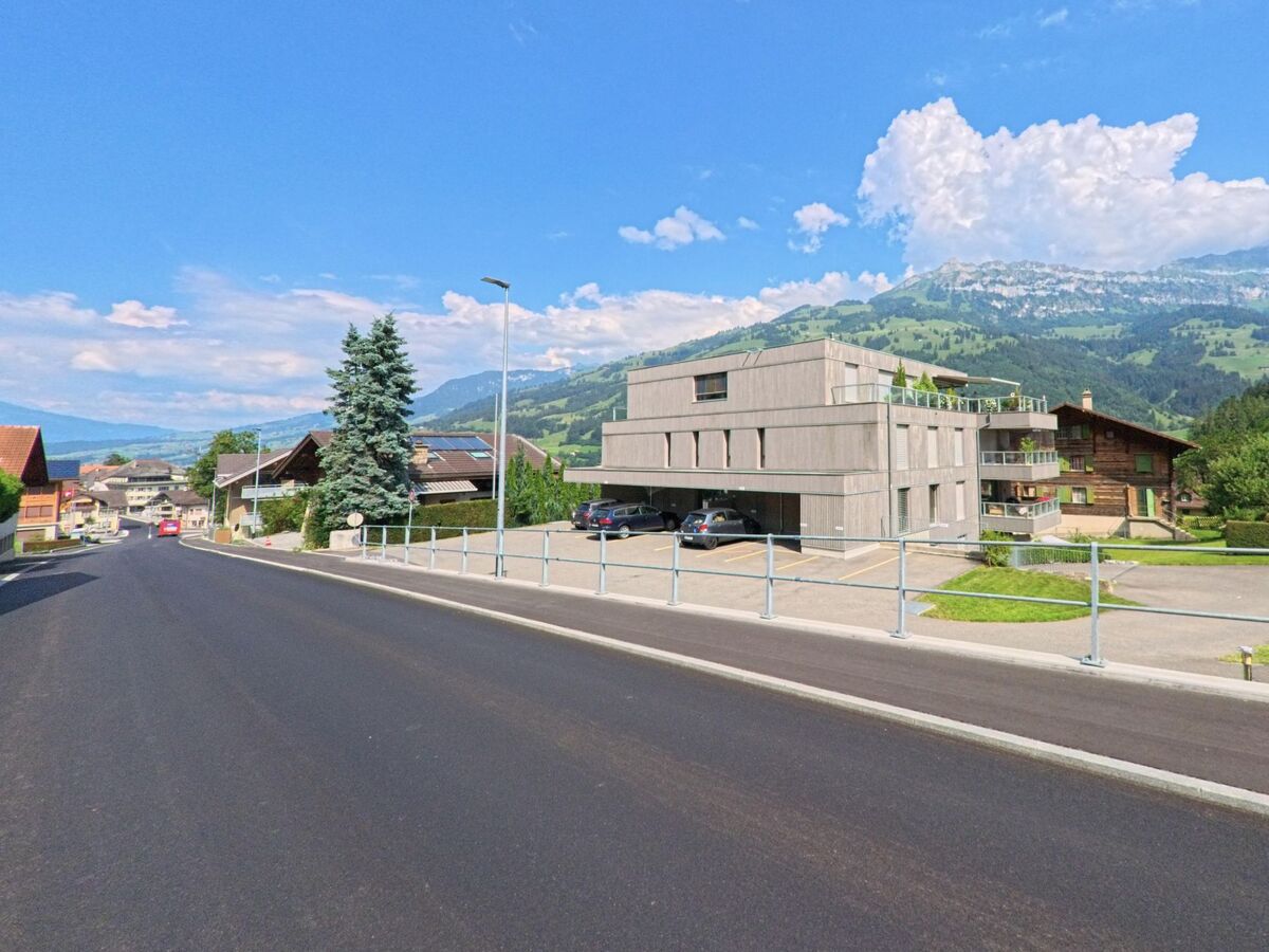  In Frutigen (3714, Kanton Bern) verläuft eine sanft abfallende Wohnstrasse entlang moderner und traditioneller Häuser mit Blick auf die grünen Berghänge.