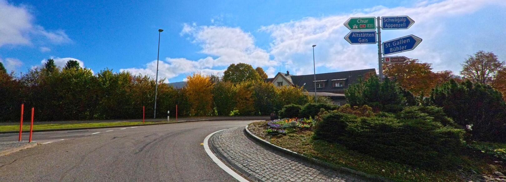 In Gais (9056, Kanton Appenzell Ausserrhoden) zeigt ein rund angelegter Verkehrsknoten vor herbstlicher Bepflanzung mehrere Wegweiser zu umliegenden Orten.