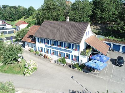 Das Gasthaus zum Schuetzen in Leibstadt (5325, Kanton Aargau) ist ein traditionelles Gebäude mit blauen Fensterläden und Blumenschmuck an der Fassade.