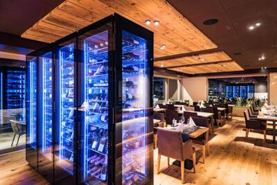 Im modernen Gastraum eines Restaurants in Lachen (8853, Kanton Schwyz) stehen gedeckte Tische neben einem grossen beleuchteten Weinschrank mit blauer Beleuchtung.