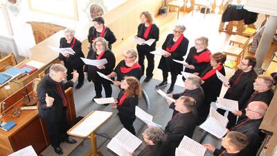 In Entlebuch singt der Gemischte Chor Entlebuch waehrend einer Probe in der Kirche, angeleitet vom Dirigenten und mit Notenblaettern in der Hand.